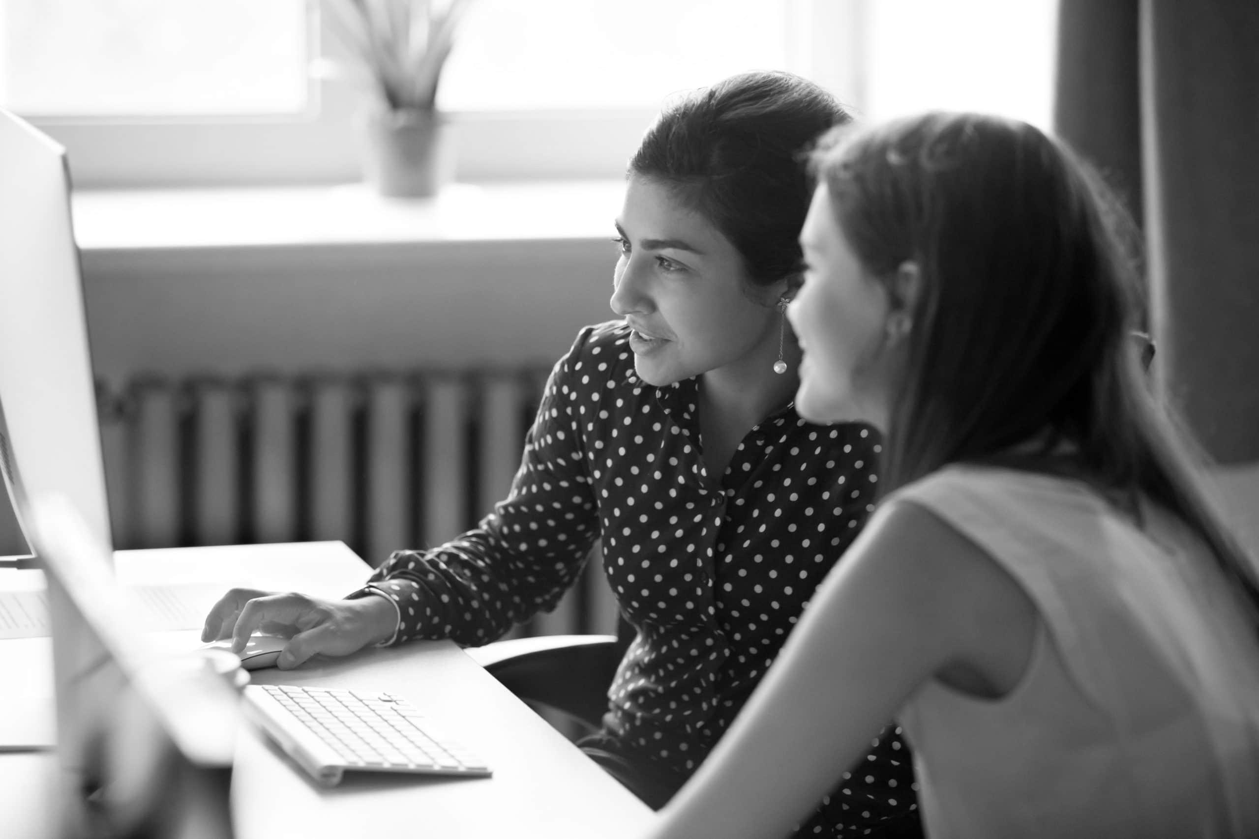 Smiling female colleagues work together at computer