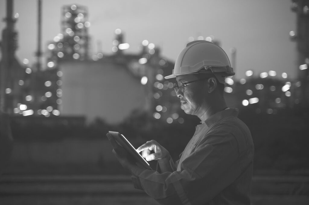 Engineer using tablet near oil refinery at night.